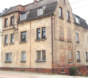 Unsaniertes Mehrfamilienhaus mit beschädigter Fassade vor der Renovierung